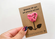 a hand holding a card with a pink heart shaped flower