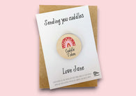 a wooden badge with the words sending you cuddles on it